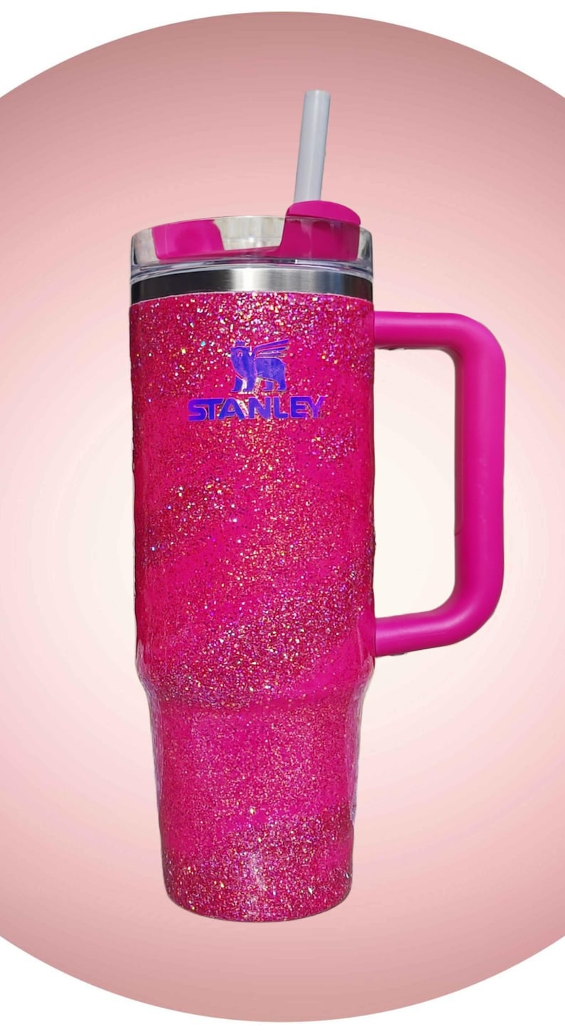 Pode incluir: Um copo Stanley rosa brilhante com uma al&ccedil;a e um canudo. O copo tem o logotipo Stanley em azul. A tampa e a al&ccedil;a s&atilde;o de cor rosa s&oacute;lida. O copo foi projetado para manter as bebidas frias ou quentes.