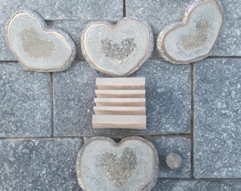 May include: A collection of heart-shaped coasters with a glittery, crystal-like center and a gold-colored trim. A small, light-colored soap dish and a coin are also present. The coasters are arranged on a gray, textured surface.