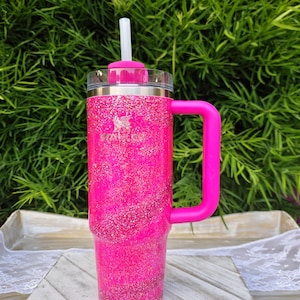 Pode incluir: Um copo rosa brilhante com glitter, com uma al&ccedil;a e canudo a condizer. O copo apresenta um log&oacute;tipo prateado e uma tampa transparente. A pega &eacute; rosa brilhante e o canudo &eacute; branco. Concebido para bebidas frias ou quentes.