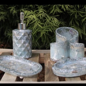 May include: A bathroom set in blue and grey with a geometric design. The set includes a soap dispenser, a toothbrush holder, two soap dishes, and a tumbler. The items are displayed on a wooden surface.