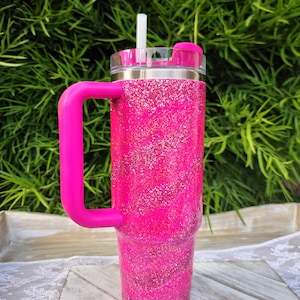 Pode incluir: Um copo rosa vibrante com glitter e uma al&ccedil;a e tampa a condizer. O copo tem uma tampa transparente com canudo e um controle deslizante rosa. A al&ccedil;a &eacute; de cor rosa brilhante. O copo est&aacute; em uma bandeja de madeira branca.