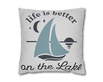 May include: A white square cushion with the text "life is better on the Lake" in black script. The cushion features a teal sailboat, a crescent moon, and a sun graphic.