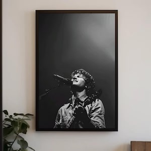 May include: Monochrome framed print of a musician performing live. The image shows a musician singing into a microphone and playing a guitar. The lighting creates a dramatic effect, highlighting the performer on stage.