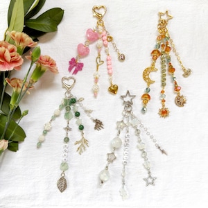 May include: Four beaded keychains with various charms, including hearts, stars, and leaves. One keychain has the word "HOAX" spelled out, another has "SHOWGIRL", and a third has "OPALUDE". The keychains feature a mix of colors, including pink, green, gold, and clear beads.