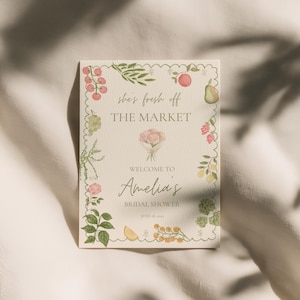 Peut inclure: Une invitation rectangulaire avec une bordure festonn&eacute;e, orn&eacute;e d'illustrations &agrave; l'aquarelle de fruits et de feuillages. Le texte indique "she's fresh off THE MARKET" et "Welcome to Amelia's Bridal Shower."
