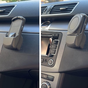 Könnte beinhalten: Eine mattschwarze Handyhalterung für das Auto, die am Armaturenbrett eines Fahrzeugs befestigt ist. Die Halterung verfügt über eine verstellbare Schale mit einer unteren Ablage und einen kreisförmigen magnetischen Befestigungspunkt an der Vorderseite.
