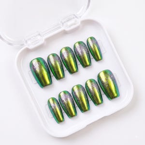 May include: A set of ten press-on nails in a white plastic storage case. Each nail features a metallic, iridescent finish that shifts between vibrant green and deep blue, accented with a fine silver glitter gradient concentrated at the base.