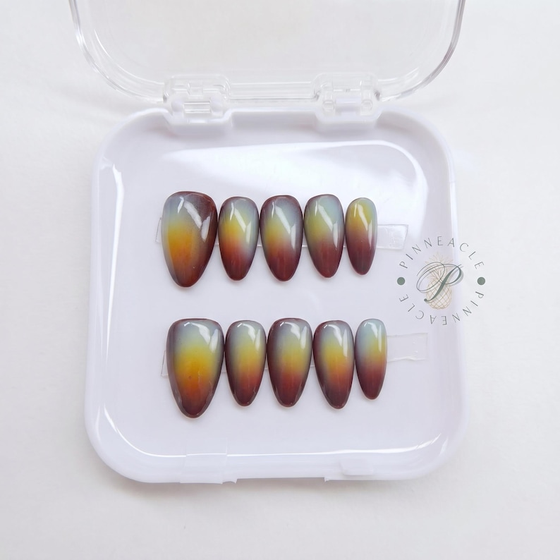 May include: A set of ten almond-shaped press-on nails arranged in two rows inside a white plastic container. Each nail features a smooth gradient transition from a deep dark brown at the base to a bright yellow and a translucent milky white tip.
