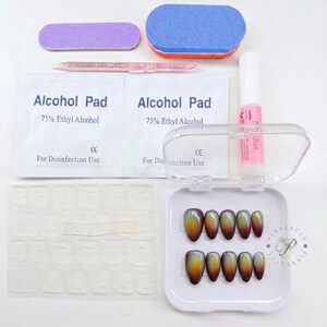 May include: A nail art kit containing ten almond-shaped press-on nails with a gradient finish transitioning from dark red to yellow, a clear plastic storage case, nail glue, two alcohol pads, a pink cuticle pusher, and a nail file and buffer.