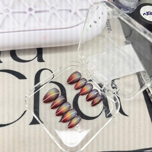 May include: A set of ten almond-shaped press-on nails featuring a gradient transition from deep red at the base to a bright yellow center and a dark gray tip, accented with a single thin white vertical line running down the center of each nail.