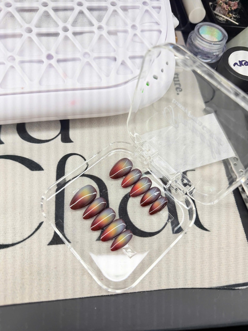 May include: A set of ten almond-shaped press-on nails featuring a gradient transition from deep red at the base to a bright yellow center and a dark gray tip, accented with a single thin white vertical line running down the center of each nail.