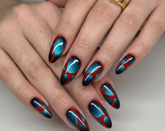 May include: Almond-shaped fingernails featuring a glossy finish with a vibrant red and metallic blue pattern resembling interconnected circular shapes. A gold-toned ring with a smooth, round black stone is worn on the ring finger of the right hand.