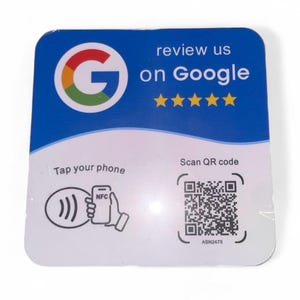 May include: A square sign with rounded corners featuring a blue and white background. It displays the Google logo, the text review us on Google, five yellow stars, a graphic showing a phone with NFC, and a QR code with the text Scan QR code.