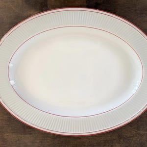 May include: A white oval serving platter with a raised, textured rim and a thin red line around the edge.