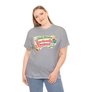 Puede incluir: Una camiseta gris con el texto "Data Driven, Emotionally Drained" en un gráfico colorido. El gráfico incluye imágenes de gráficos, un gráfico circular, una lupa y una carpeta. La camiseta está hecha de un material suave.