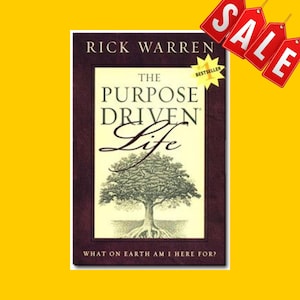 以下が含まれることがあります： リック・ウォレン著「The Purpose Driven Life」というタイトルの本。表紙には木のイラストと「What on Earth Am I Here For?」というテキストが描かれています。「Bestseller」のステッカーと赤い「SALE」タグが見えます。