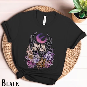 May include: Black t-shirt featuring a floral design and a purple and pink symbol with the text "This is the way" in a stylised font.