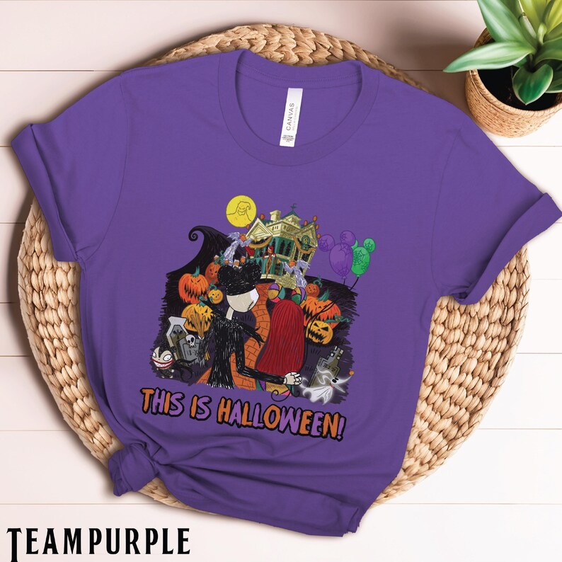 Puede incluir: Una camiseta morada con un dise&ntilde;o de Halloween. El dise&ntilde;o incluye a Jack Skellington, Sally, calabazas, una casa embrujada y el texto "THIS IS HALLOWEEN!". La camiseta est&aacute; hecha de un material suave.