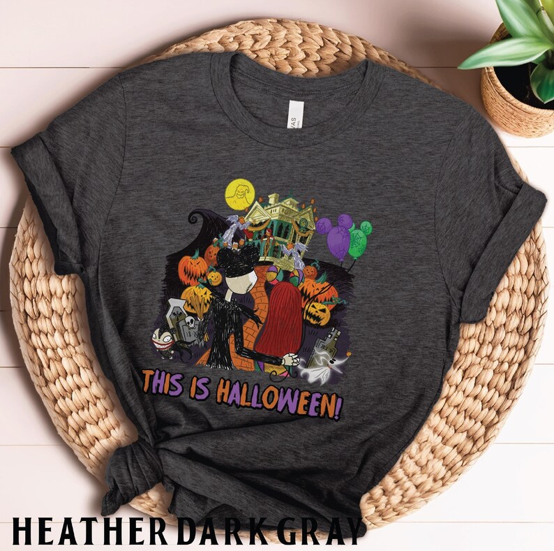 Puede incluir: Camiseta gris oscuro con un dise&ntilde;o de Halloween. El dise&ntilde;o incluye a Jack Skellington y Sally, calabazas, una casa embrujada y el texto "THIS IS HALLOWEEN!". Una camiseta divertida para Halloween. Hecha de material gris oscuro.