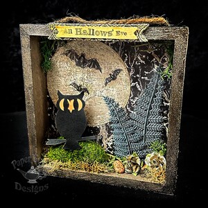 May include: A Halloween-themed shadow box with a wooden frame. Inside, a full moon with bats, a black owl, and a fern are set against a dark background. The text "All Hallows' Eve" is displayed on a banner.