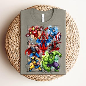 May include: A grey t-shirt with a vibrant graphic of Marvel superheroes, such as Iron Man, Captain America, Spider-Man, Thor, Wolverine, Hulk, and Deadpool. The design is set against a watercolour-style background.