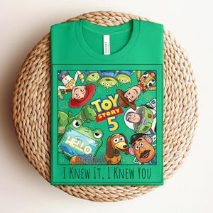 K&ouml;nnte beinhalten: Ein leuchtend gr&uuml;nes T-Shirt mit einem Grafikdruck von Toy Story-Figuren, darunter Woody, Buzz Lightyear, Jessie, Rex, Slinky Dog, Mr. Potato Head und Aliens. Der Text lautet Toy Story 5 und I KNEW IT, I KNEW YOU.