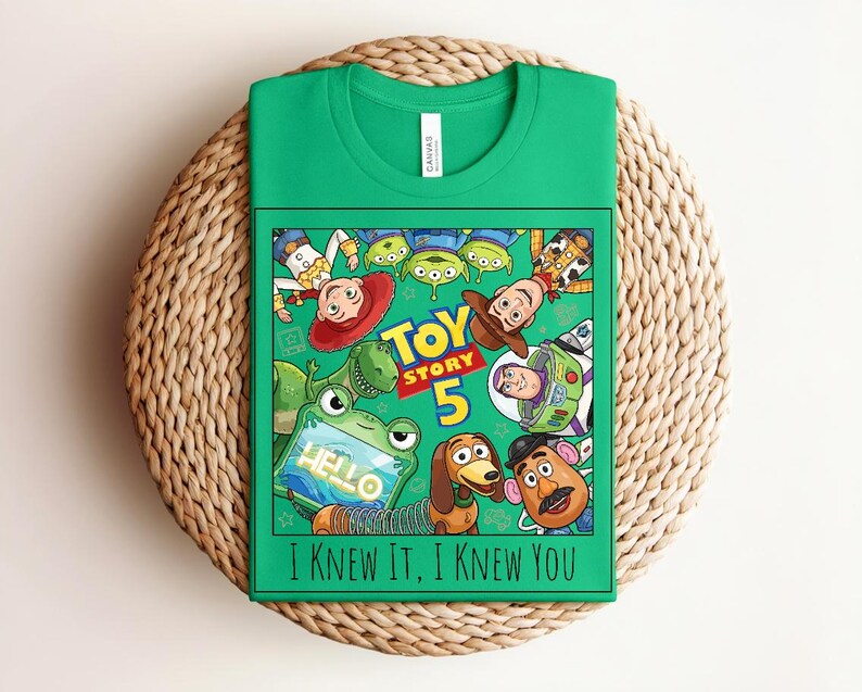 K&ouml;nnte beinhalten: Ein leuchtend gr&uuml;nes T-Shirt mit einem Grafikdruck von Toy Story-Figuren, darunter Woody, Buzz Lightyear, Jessie, Rex, Slinky Dog, Mr. Potato Head und Aliens. Der Text lautet Toy Story 5 und I KNEW IT, I KNEW YOU.