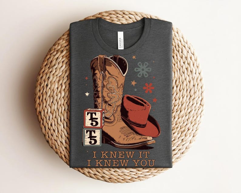 May include: A dark gray t-shirt featuring a graphic of a brown leather cowboy boot, a red cowboy hat, and two stacked blocks with the text T5. The shirt includes the text I KNEW IT I KNEW YOU below the graphic, along with small star and flower icons.