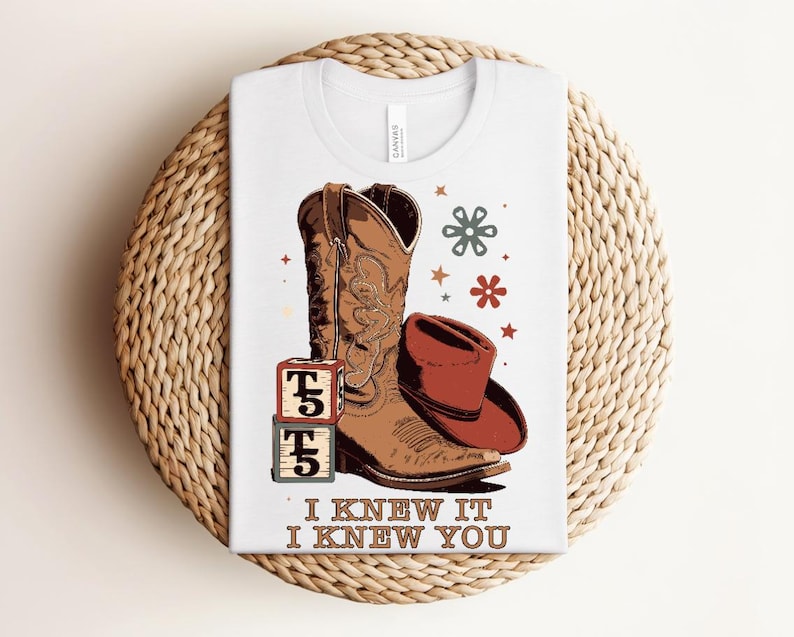 May include: A white t-shirt featuring a graphic of a brown cowboy boot, a red cowboy hat, two stacked alphabet blocks with the letter T, and small star and flower icons. The text "I KNEW IT I KNEW YOU" is printed in brown at the bottom.