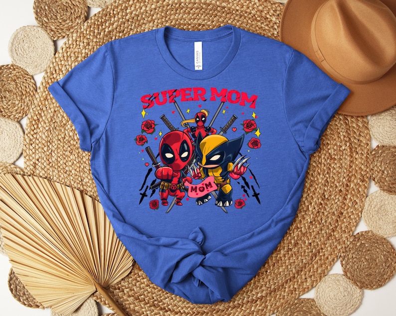 K&ouml;nnte beinhalten: Blaues T-Shirt mit einer Grafik von Deadpool und Wolverine und dem Text "SUPER MOM". Das Design umfasst Rosen, Schwerter und das Wort "MOM" auf einem Banner. Das T-Shirt hat einen Rundhalsausschnitt.