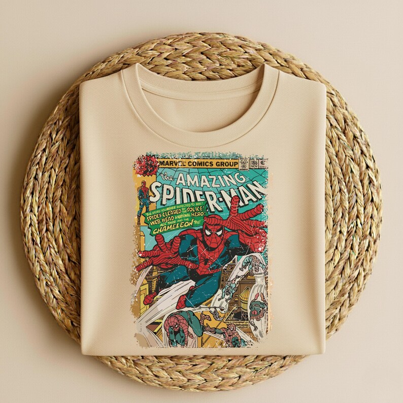 May include: A beige t-shirt featuring a vintage comic book cover of The Amazing Spider-Man. The comic art shows Spider-Man in a dynamic pose with red and blue costume, with text that reads "MARVEL COMICS GROUP" and "SPIDER-MAN".