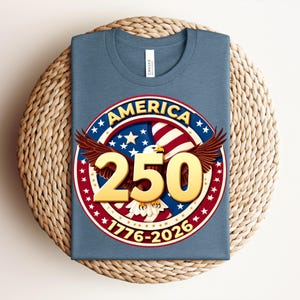 May include: A blue t-shirt with a circular graphic commemorating the 250th anniversary of America. The graphic features a red, white, and blue design with an eagle, stars, and the text "AMERICA 250 1776-2026."