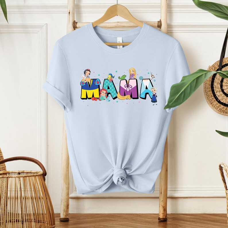 K&ouml;nnte beinhalten: Hellblaues T-Shirt mit einem Aufdruck von Disney-Prinzessinnen, die das Wort "MAMA" buchstabieren.
