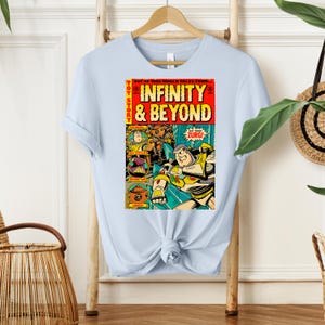 Puede incluir: Una camiseta azul claro con un dise&ntilde;o de c&oacute;mic vintage con Buzz Lightyear de Toy Story. La portada del c&oacute;mic dice "Toy Story Infinity & Beyond" con una imagen de Buzz Lightyear con un traje espacial y otros personajes de la pel&iacute;cula.