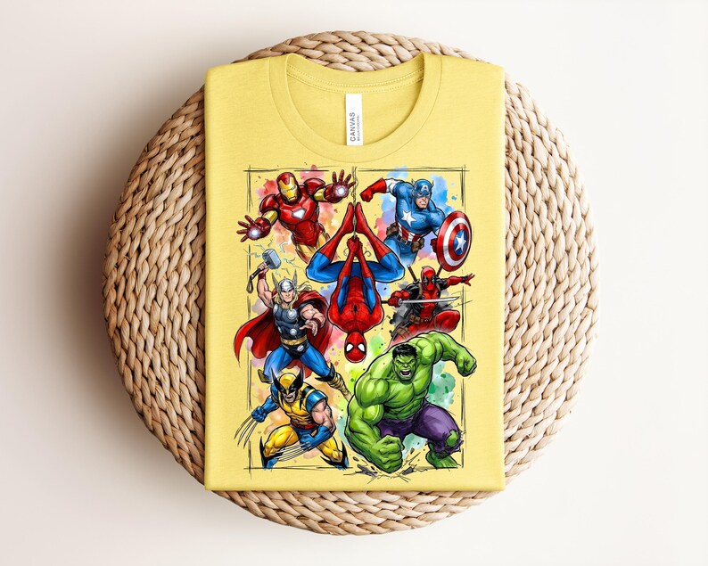 May include: A folded yellow t-shirt with a vibrant graphic of Marvel superheroes such as Iron Man, Captain America, and Spider-Man. The design is framed within a rectangle. The shirt rests on a circular woven mat.