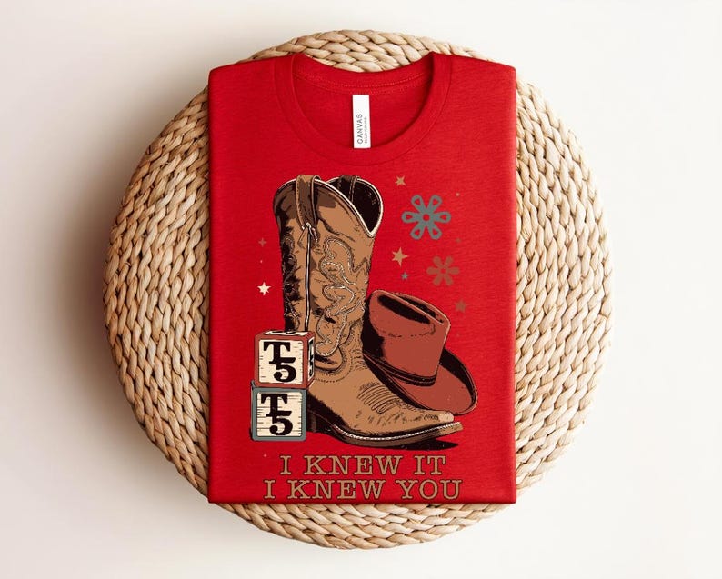 May include: A red t-shirt featuring a graphic of a brown cowboy boot, a brown cowboy hat, and two stacked alphabet blocks with the letter T and the number 5. The design includes small star and flower icons and the text I KNEW IT I KNEW YOU.