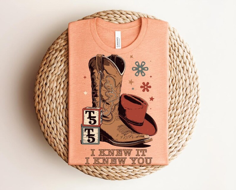 May include: A peach-colored t-shirt featuring a graphic of a brown cowboy boot, a brown cowboy hat, and two stacked blocks with the letter T and the number 5. The text "I KNEW IT I KNEW YOU" is printed below the graphic with small flower icons.