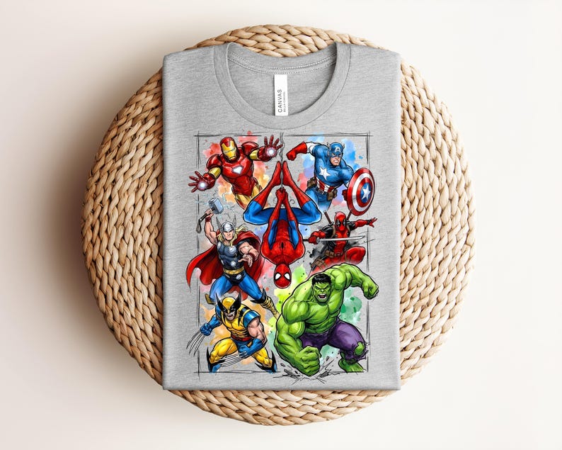 May include: A grey t-shirt with a graphic of Marvel superheroes. The design includes Iron Man, Captain America, Spider-Man, Thor, Wolverine, Hulk, and Deadpool. The superheroes are depicted in action poses with bright colours and detailed illustrations.