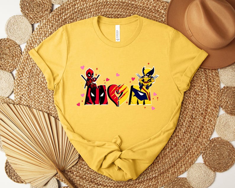 Op de afbeelding: Mosterdgele t-shirt met een afbeelding van Deadpool en Wolverine. Het ontwerp bevat het woord "Love" met hartaccenten. Het t-shirt is gemaakt van zacht materiaal en heeft een klassieke ronde hals.