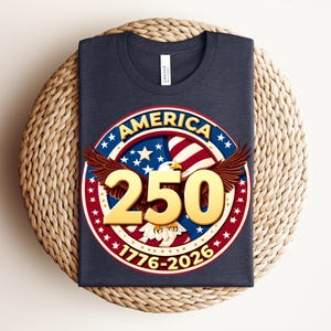 May include: A navy blue t-shirt with a circular graphic featuring the word "AMERICA", stars, stripes, and the number "250" in gold. The graphic includes an eagle and the dates "1776-2026".