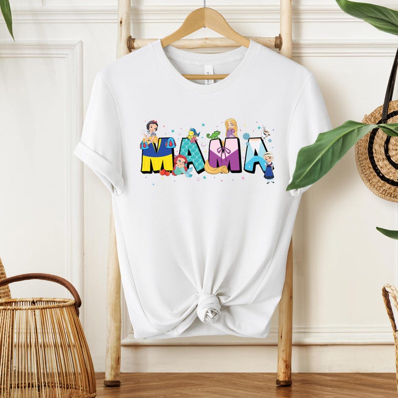 K&ouml;nnte beinhalten: Wei&szlig;es T-Shirt mit einer Grafik von Disney-Prinzessinnen, die das Wort "MAMA" buchstabieren.