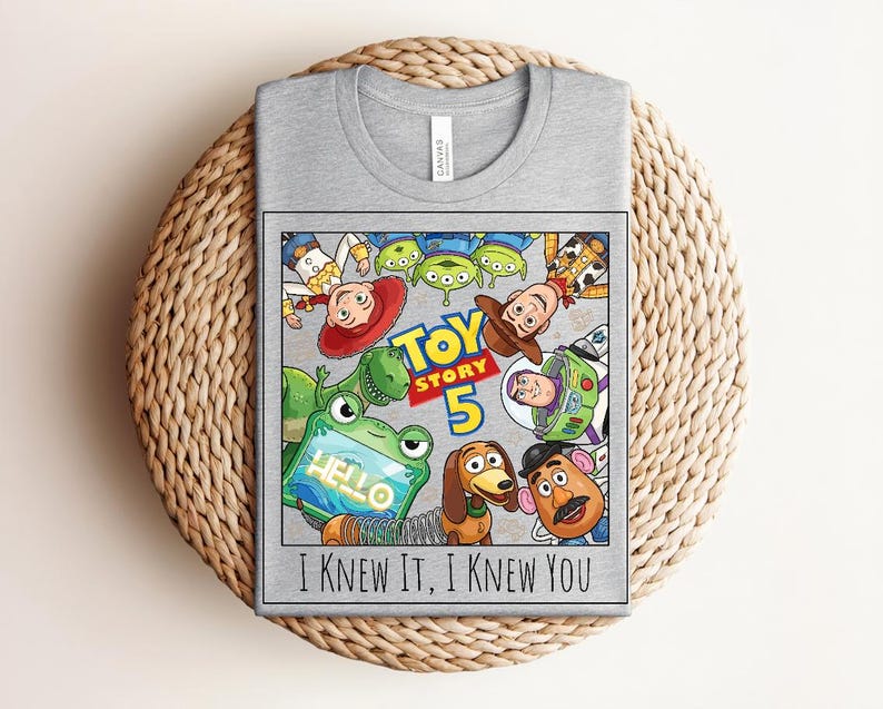 K&ouml;nnte beinhalten: Ein graues T-Shirt mit einem Grafikdruck von Toy Story-Figuren, darunter Woody, Buzz Lightyear, Jessie, Rex, Slinky Dog, Mr. Potato Head und Aliens. Der Text lautet Toy Story 5 und I KNEW IT, I KNEW YOU.