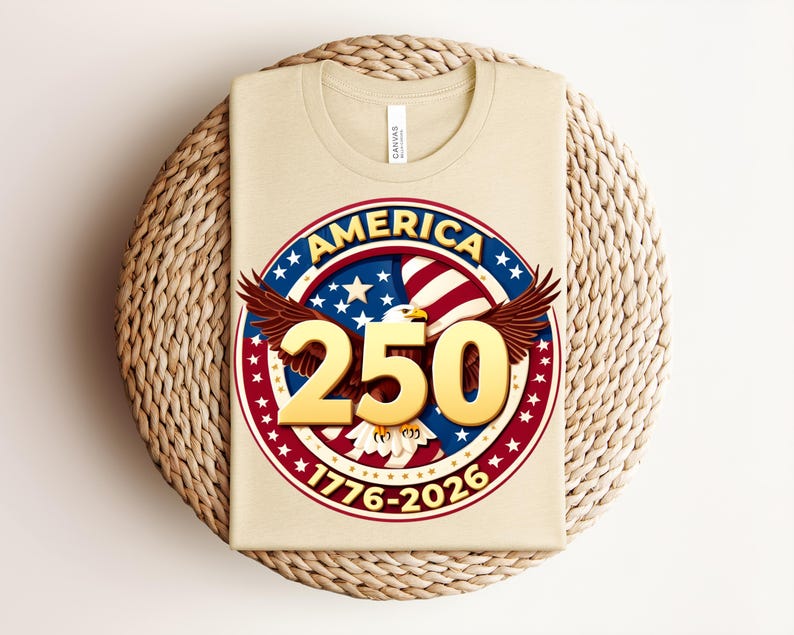 May include: A beige t-shirt with a circular graphic featuring the word "AMERICA" in a red and blue design, with the number "250" in gold. The graphic includes an eagle, stars, and the years "1776-2026".