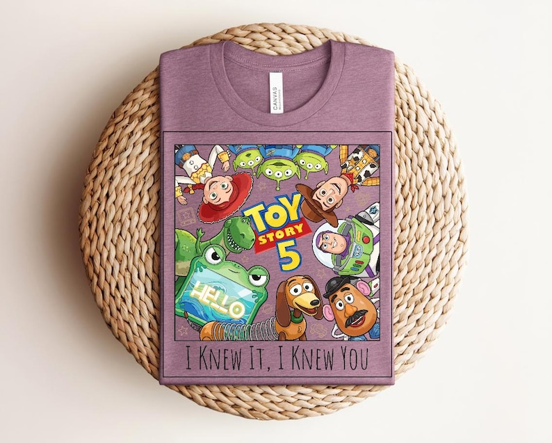 K&ouml;nnte beinhalten: Ein malvenfarbenes T-Shirt mit Rundhalsausschnitt und einem Grafikdruck von Toy Story-Figuren, darunter Woody, Buzz Lightyear, Jessie, Rex, Slinky Dog, Mr. Potato Head und Aliens. Der Text lautet Toy Story 5 und I KNEW IT, I KNEW YOU.