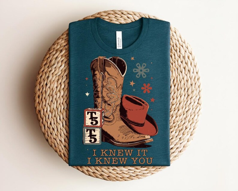 May include: A dark teal t-shirt featuring a graphic of a brown cowboy boot, a brown cowboy hat, and two stacked alphabet blocks with the letter T and the number 5. The text "I KNEW IT I KNEW YOU" is printed below the graphic with small star and flower icons.