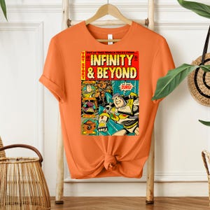 Puede incluir: Camiseta naranja con un dise&ntilde;o de c&oacute;mic vintage con personajes de la franquicia de pel&iacute;culas Toy Story. La portada del c&oacute;mic dice "Toy Story Infinity & Beyond" con una imagen de Buzz Lightyear y otros personajes.