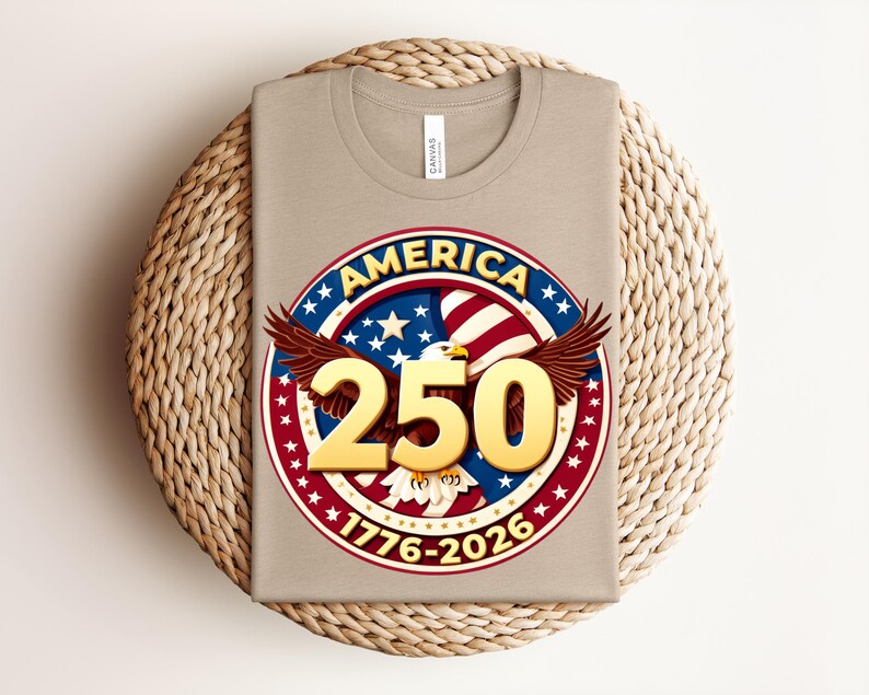May include: A beige t-shirt with a circular graphic celebrating America's 250th anniversary. The design includes an eagle, stars, and the text "AMERICA 250 1776-2026" in red, white, and blue colours.