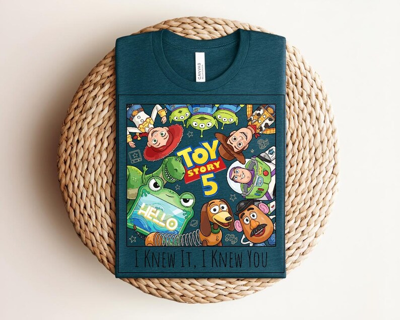 K&ouml;nnte beinhalten: Ein dunkelblaugr&uuml;nes T-Shirt mit einem Grafikdruck von Toy Story-Figuren, darunter Woody, Buzz Lightyear, Jessie, Rex, Slinky Dog, Mr. Potato Head und Aliens. Der Text lautet "TOY STORY 5", "HELLO" und "I KNEW IT, I KNEW YOU".
