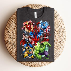 May include: Dark grey t-shirt with a vibrant graphic of Marvel superheroes, such as Iron Man, Spider-Man, Captain America, Thor, Wolverine, Deadpool, and the Hulk. The tee is made of a soft material and is suitable for casual wear.