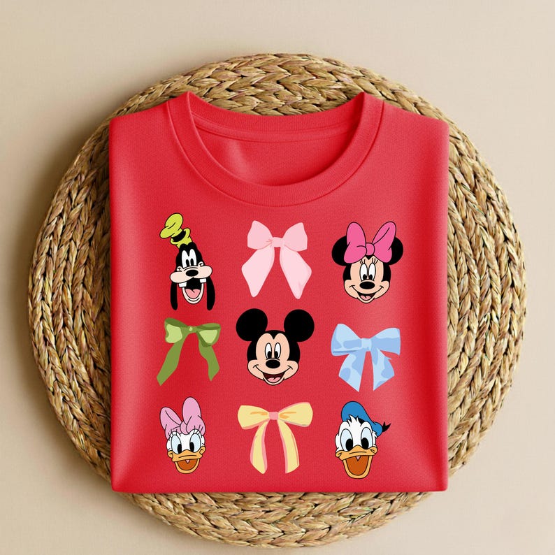 May include: A red crew neck sweatshirt with cartoon character faces and bows. Characters include Mickey Mouse, Minnie Mouse, Donald Duck, Daisy Duck, and Goofy. The bows are in various colours, including pink, green, and yellow.